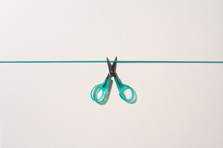 A small pair of green scissors opens to cut a green cord.