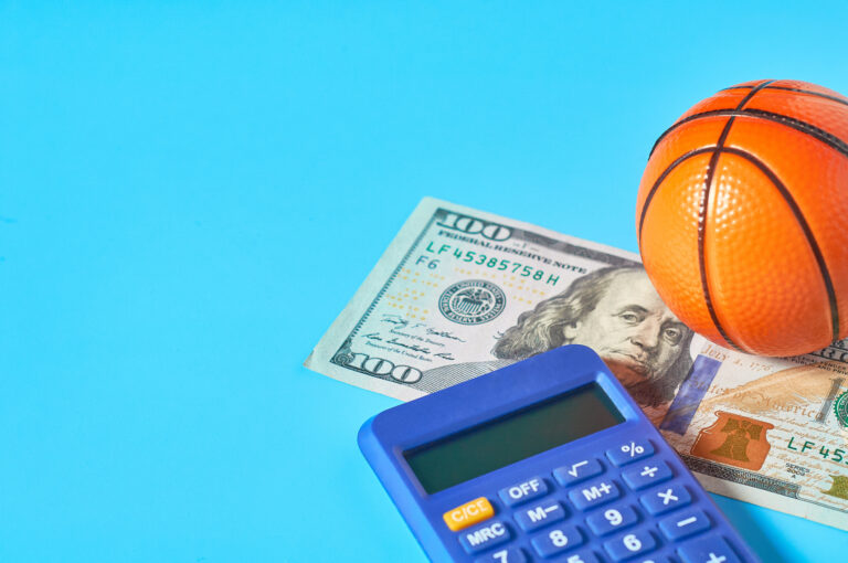 Basketball, calculator, and one hundred dollar bill on a bright blue background