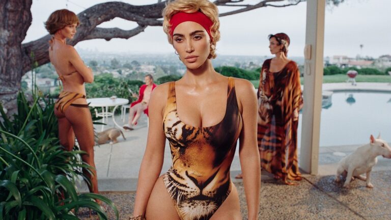 kim kardashian standing in a tiger-printed swimsuit with a red hairband, in front of two women and a dog outside