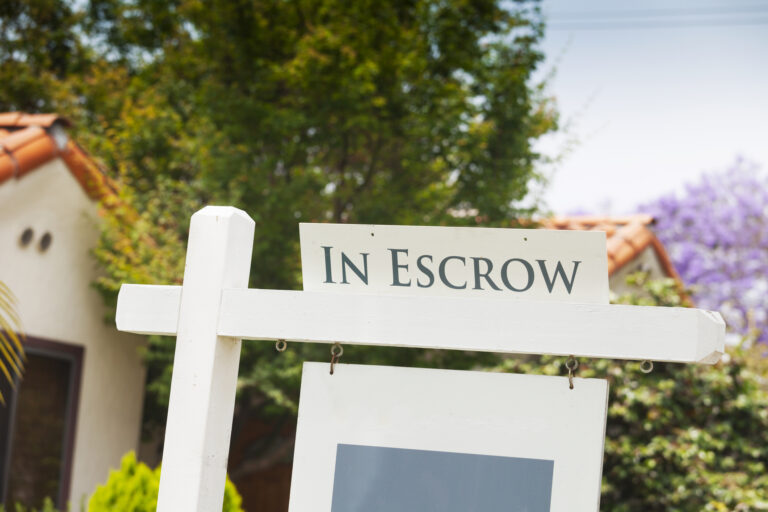 A sign reading &quot;in escrow&quot; on top of a &quot;for-sale&quot; sign at a house.