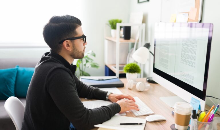 Hispanic young male writer with glasses sitting at his desk and writing his next book on the computer