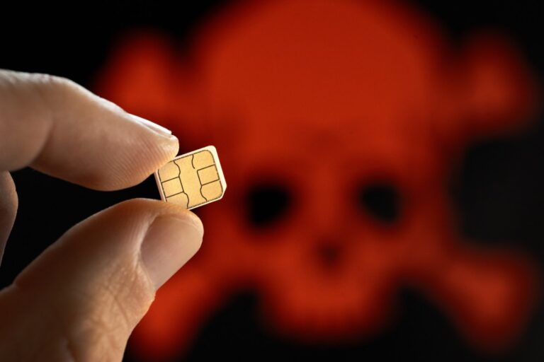 A close up shot of a person holding a SIM card, with a skull in the background to demonstrate SIM hack