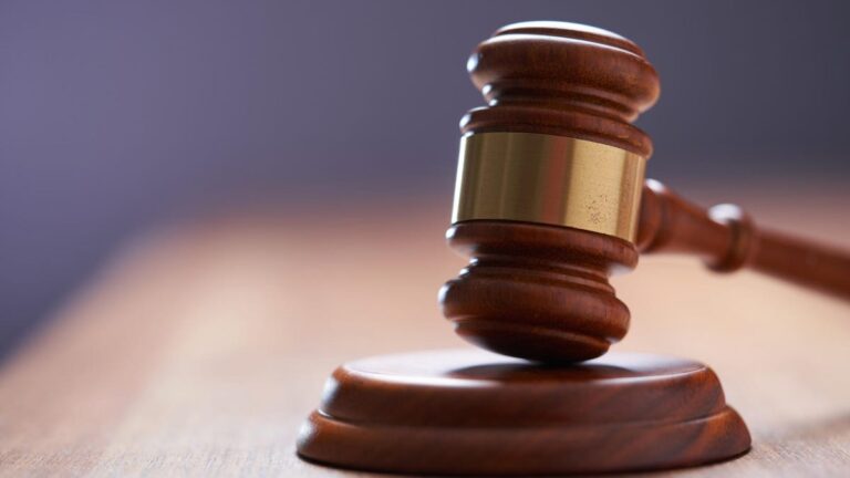 Brown judge&apos;s gavel in focus against a blurred courtroom background.
