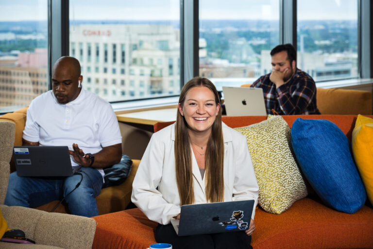 Three people sit on an orange couch and work on laptops.