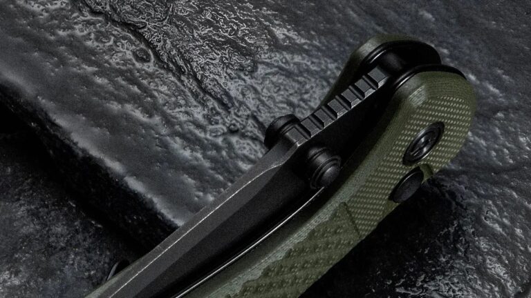 Civivi’s Tactically Styled, Multi-Deploying New EDC Knife Looks Way Too Good for Its Price Close-up of a folding knife with a textured green handle and a black blade, resting on a dark, textured surface. The knife features a thumb stud and a ridged spine for grip.