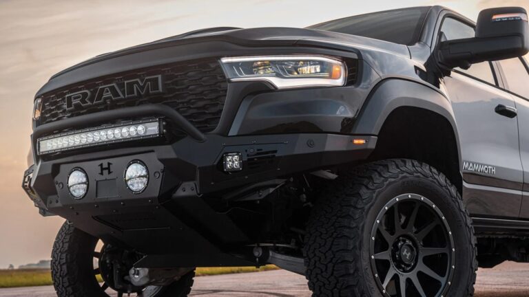 Front side view of a black and white RAM Mammoth pickup truck with large off-road tires, a heavy-duty black front bumper equipped with multiple LED lights, and a prominent RAM grille. The truck has a rugged, lifted stance suitable for off-road driving.