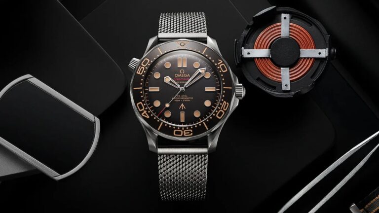 Omega Seamaster wristwatch with a black dial, beige hour markers, and a stainless steel mesh strap, displayed on a black surface alongside a copper coil component.