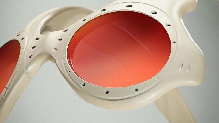 Close-up of a pair of sunglasses with a beige frame and large round orange-tinted lenses. The frame has small circular holes around the lenses and a smooth, slightly curved design.