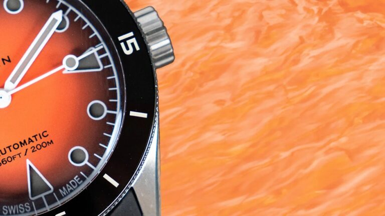 Close-up of a wren watch face with an orange gradient dial, black bezel, and white markings. The dial shows