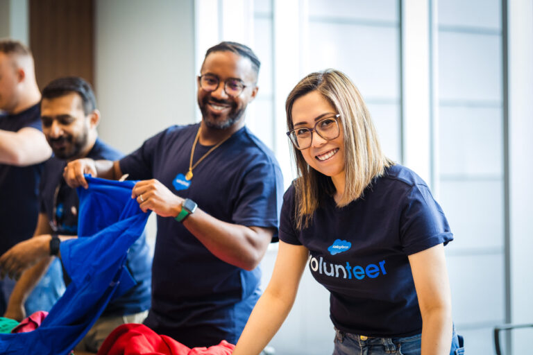 Two Salesforce employees wearing "Volunteer" shirts pack drawstring bags as part of a VTO event.