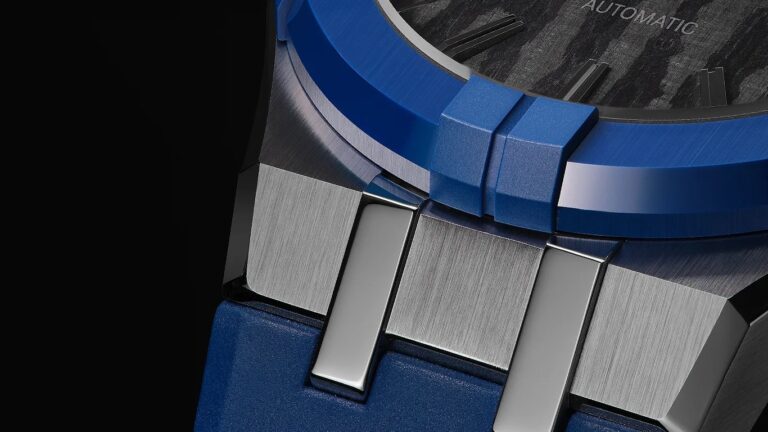 Close-up of a maurice lacroix watch featuring a blue bezel and strap, with a brushed metal case and polished metal links connecting the strap to the case. The watch dial is partially visible, showing a textured pattern and the word