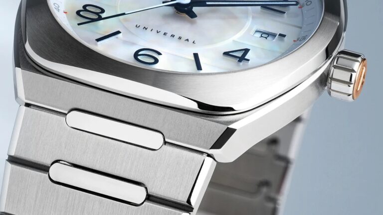 Close-up of a stainless steel wristwatch with a brushed metal bracelet and a polished bezel. The watch face features black numerals and hands, a date window, and the word