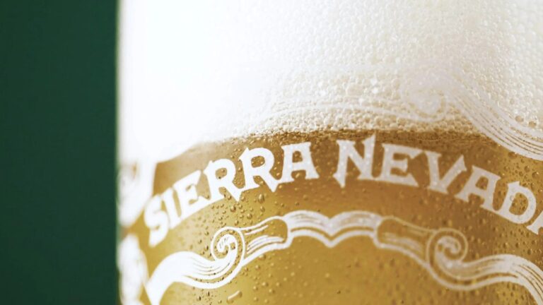 Close-up of a cold glass of Sierra Nevada beer with condensation droplets on the glass and a thick, foamy head on top. The text