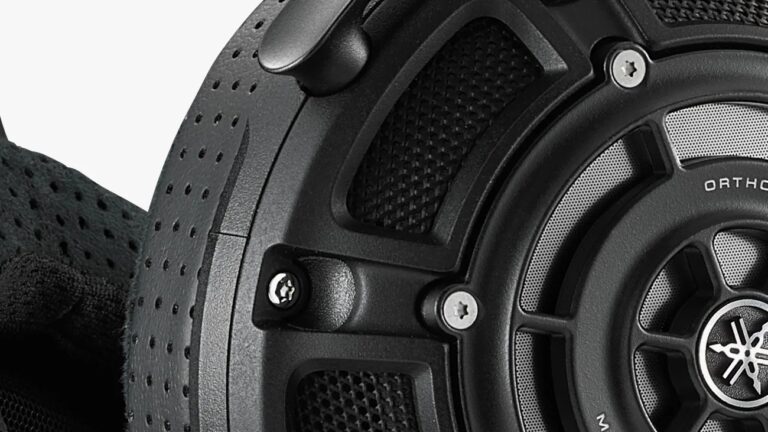 Close-up of a black headphone ear cup showing a textured, perforated outer surface, metal screws, and a mesh-covered speaker grille with part of the Yamaha logo visible.