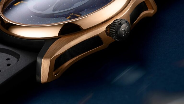 Close-up of a luxury Moser watch featuring a rose gold case with black textured inlays on the lugs, a black crown engraved with the letter
