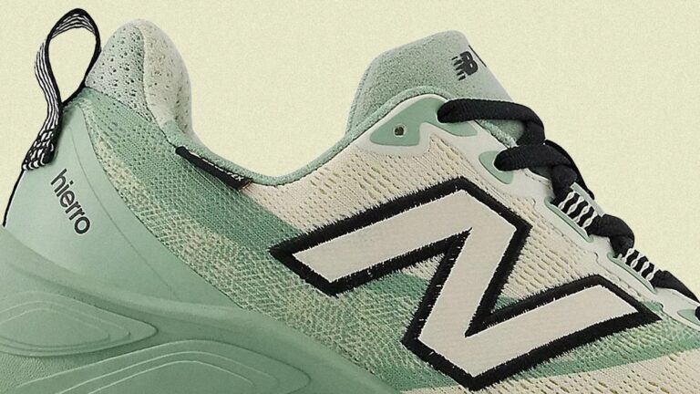 Close-up of a New Balance running shoe in light green and white with black accents. The shoe features a large white