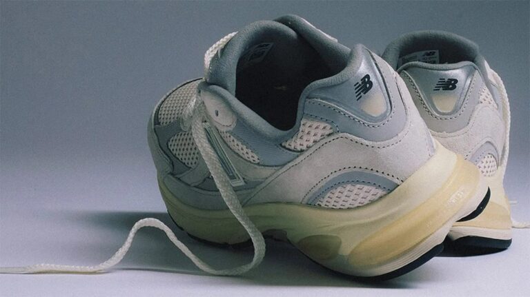 Pair of light gray and white New Balance sneakers with mesh and suede detailing, featuring white laces and a slightly yellowed sole, positioned with the heels facing forward.