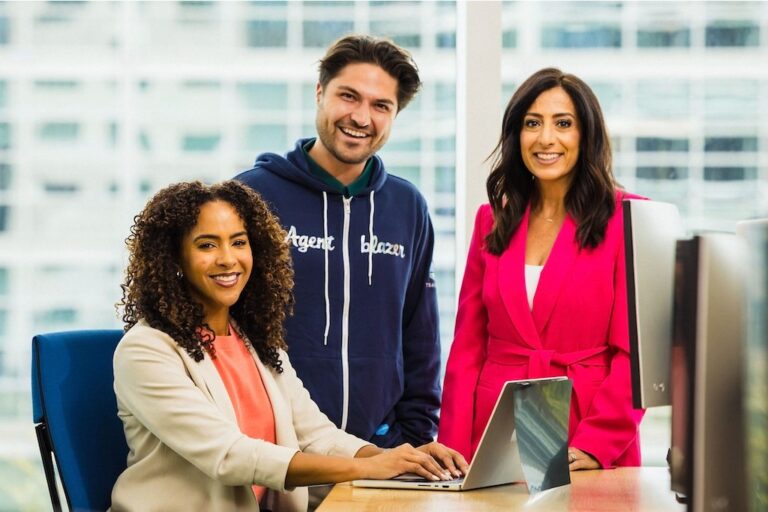 Three Salesforce employees are smiling and collaborating in a modern office setting.