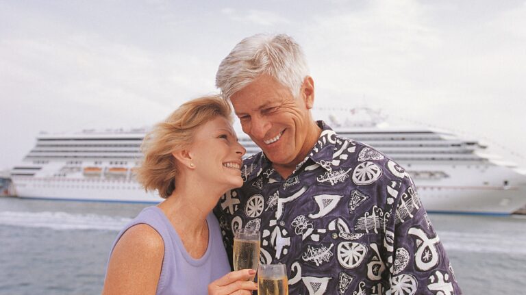 The Five Best Cruise Lines for Retirees A mature couple on a cruise stand in front of their boat.